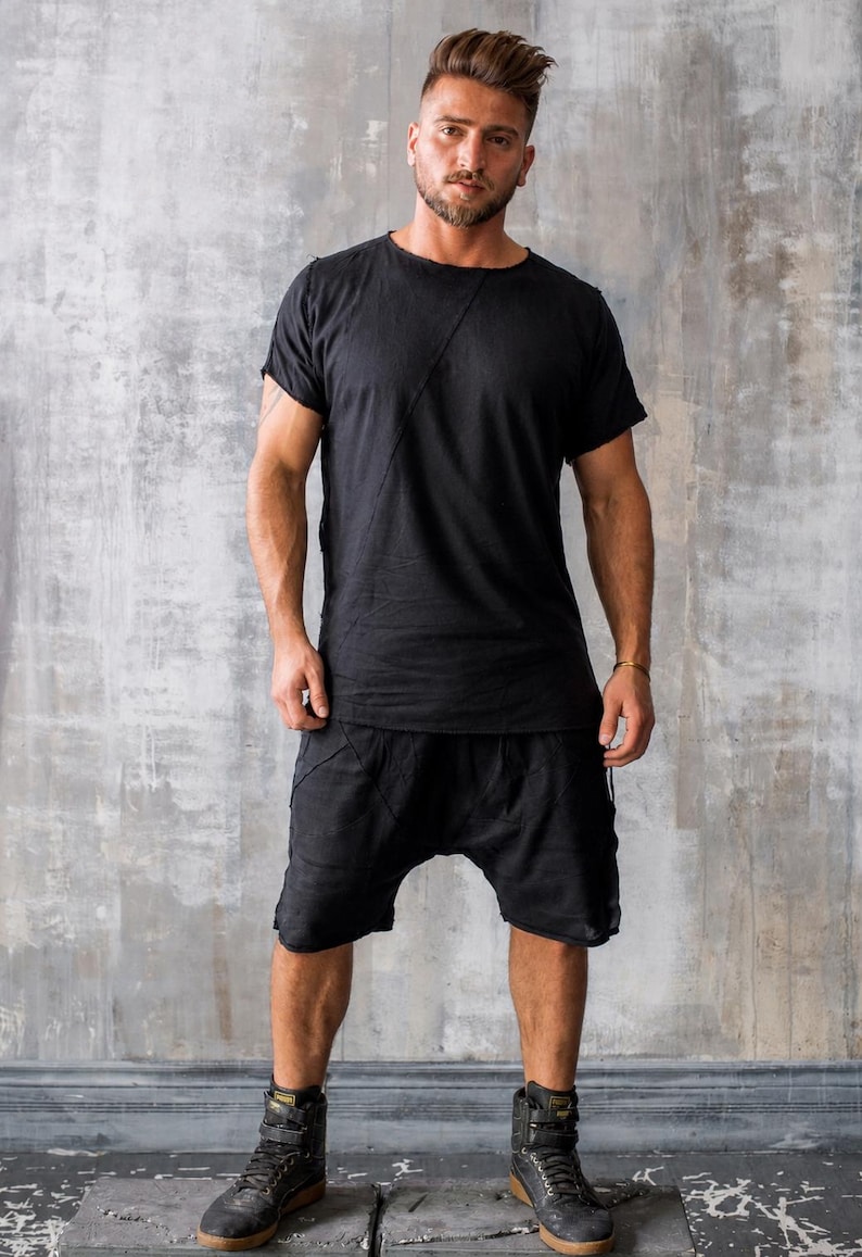 May include: Black t-shirt and shorts outfit. The short-sleeved shirt has a diagonal seam across the chest. The shorts are loose-fitting. The person is wearing black high-top boots with straps.