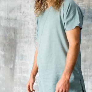 May include: A light blue linen tunic and matching trousers. The tunic has short sleeves and a split hem. The outfit is made of a soft, flowing fabric. The model is wearing a ring.
