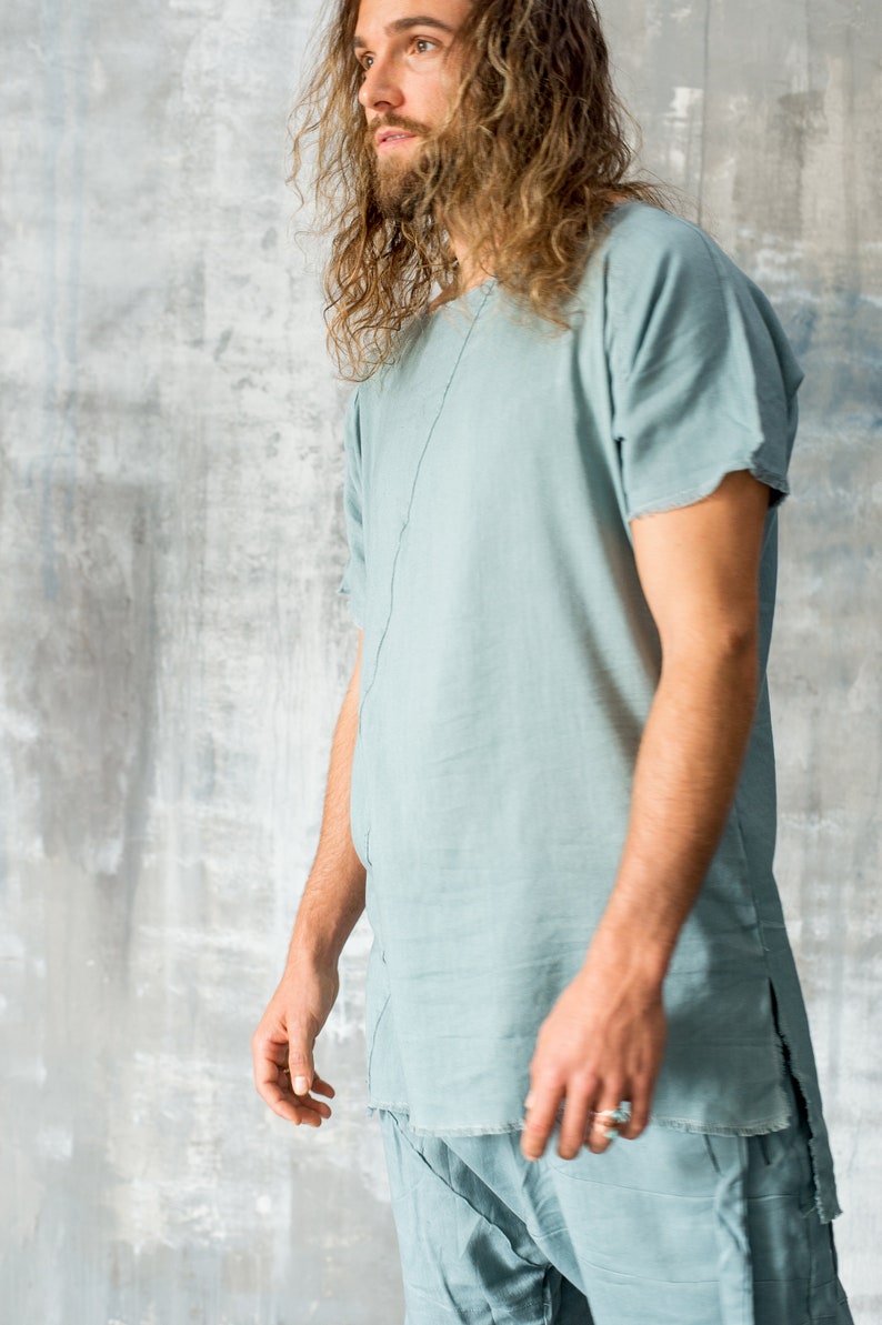 May include: A light blue linen tunic and matching trousers. The tunic has short sleeves and a split hem. The outfit is made of a soft, flowing fabric. The model is wearing a ring.