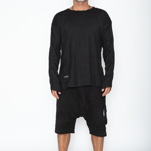 May include: Black long-sleeve shirt and matching shorts. The shirt has a raw edge neckline and a diagonal seam across the chest. The shorts have a drop-crotch design. The outfit is made of a soft, textured fabric.