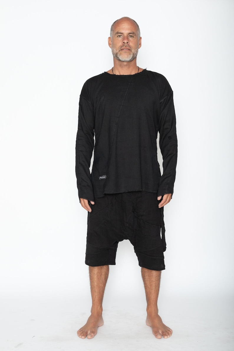 May include: Black long-sleeve shirt and matching shorts. The shirt has a raw edge neckline and a diagonal seam across the chest. The shorts have a drop-crotch design. The outfit is made of a soft, textured fabric.