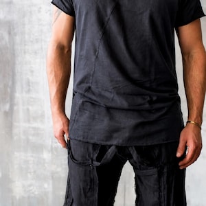 May include: Black t-shirt and shorts set. The short-sleeved shirt has a raw edge neckline and a diagonal seam. The shorts have straps and pockets. The outfit is made of a soft, dark fabric.