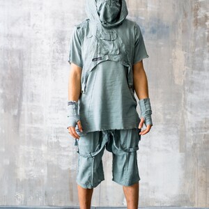 May include: A light blue outfit featuring a hooded top with pockets, shorts with straps, and fingerless gloves. The model wears sunglasses and combat boots. The outfit has a distressed, post-apocalyptic aesthetic.