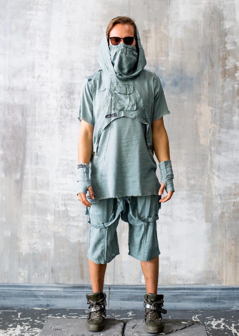 May include: A light blue outfit featuring a hooded top with pockets, shorts with straps, and fingerless gloves. The model wears sunglasses and combat boots. The outfit has a distressed, post-apocalyptic aesthetic.