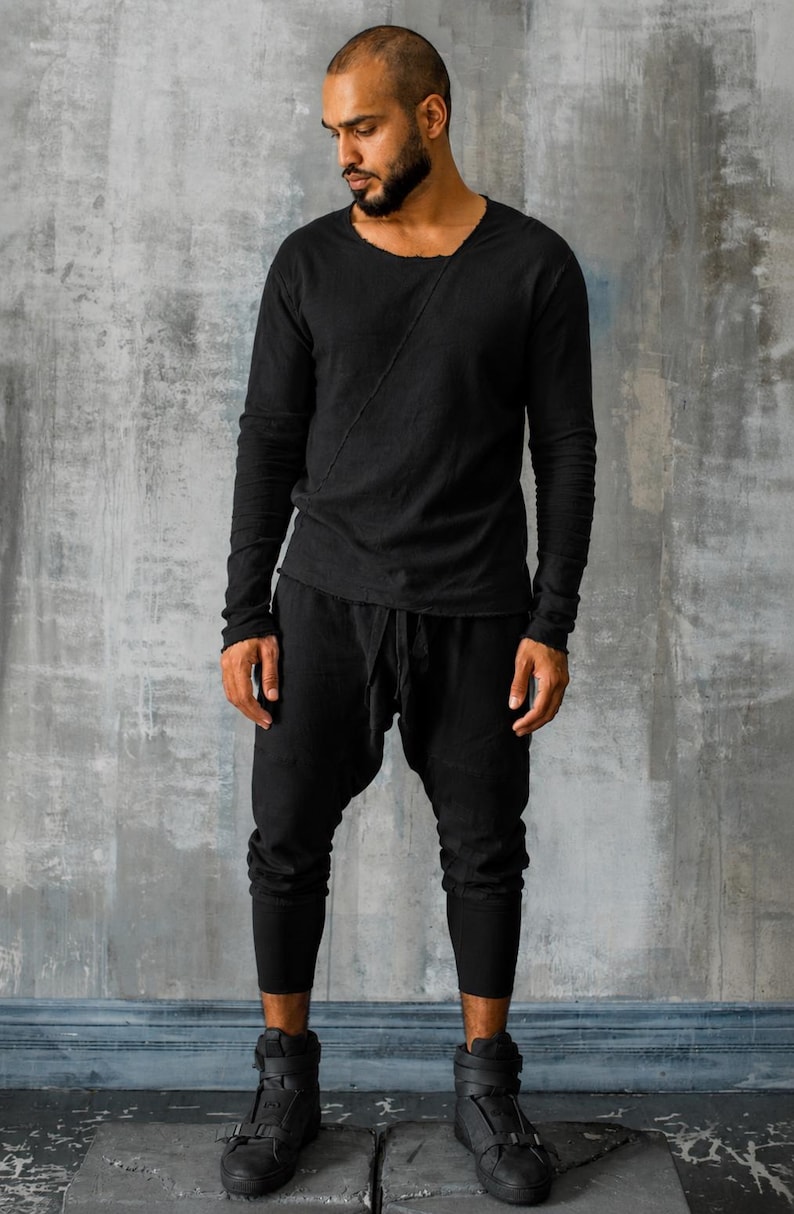 May include: A person wearing a black long-sleeve shirt with a unique neckline and black pants. The outfit is completed with black high-top sneakers. The clothing appears to be made of a soft, flowing material.