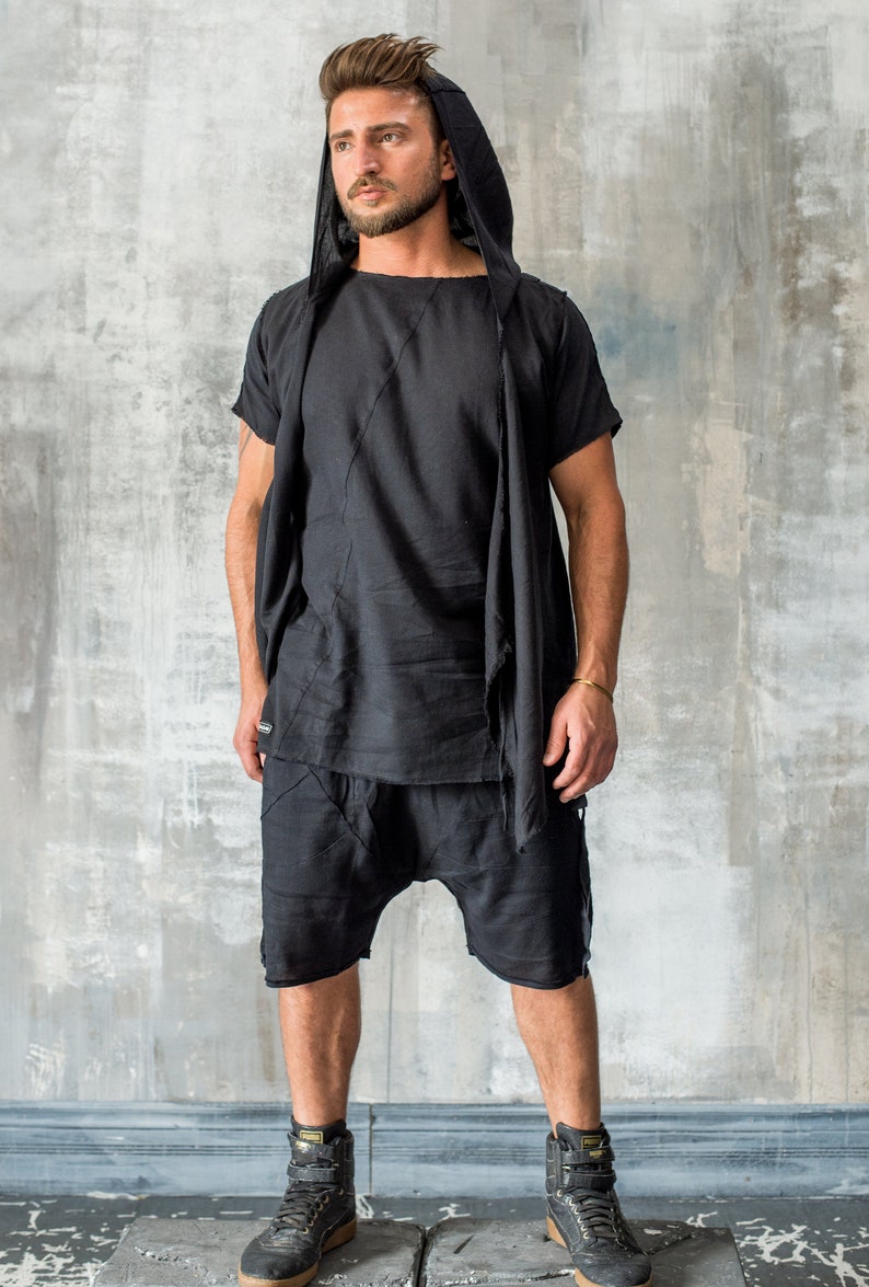 May include: A black hooded top with a long, flowing scarf. The top has a short sleeve and a relaxed fit. The model is wearing black shorts and black trainers.