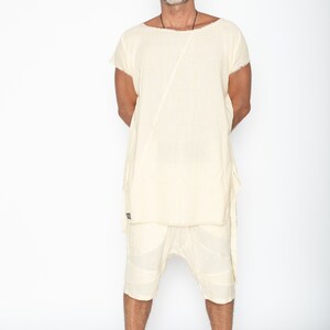 Puede incluir: Un conjunto de t&uacute;nica y pantal&oacute;n corto de lino color crema. La t&uacute;nica tiene mangas cortas y una costura diagonal &uacute;nica. El pantal&oacute;n corto llega a la rodilla con un dise&ntilde;o de patchwork. El conjunto lo lleva una persona sobre fondo blanco.