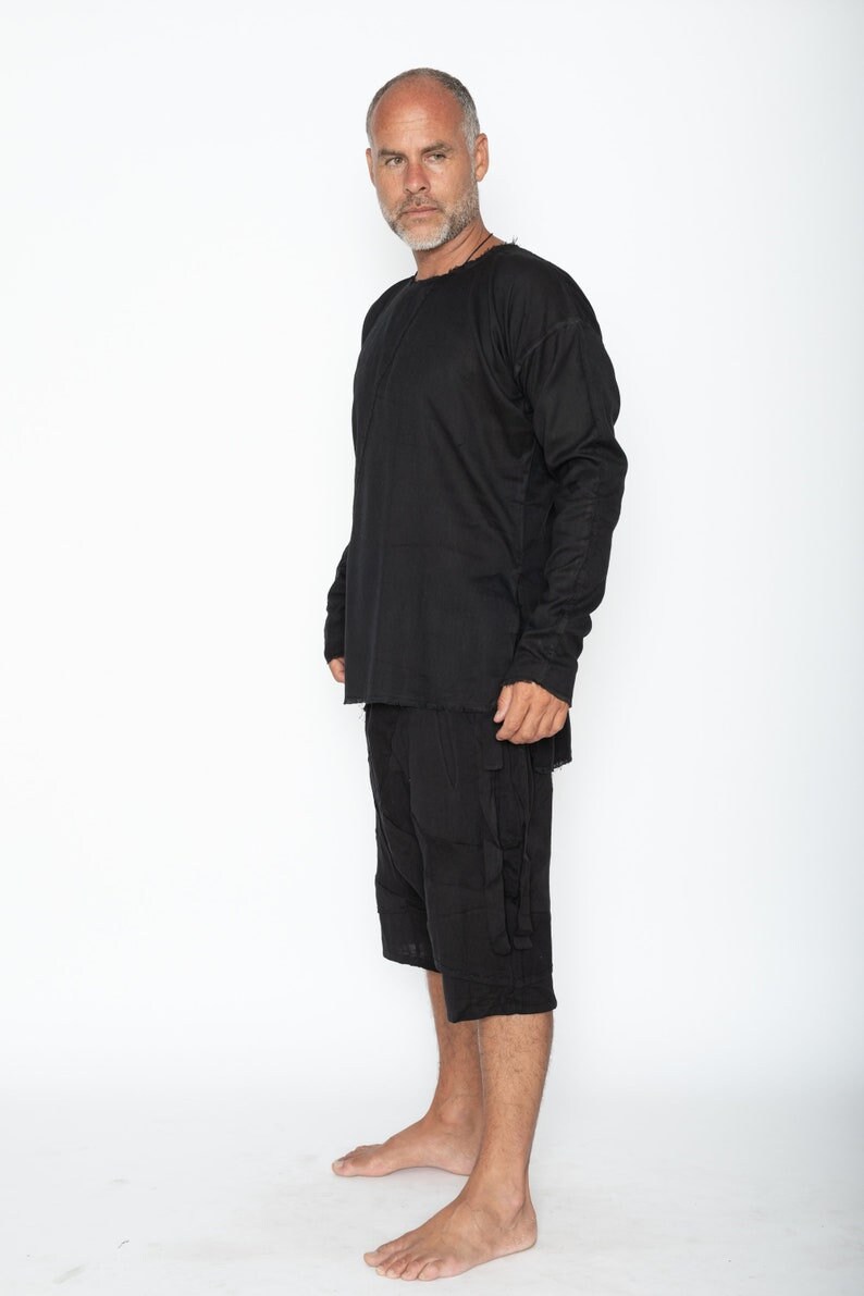 May include: Black long-sleeve shirt and matching shorts. The shirt has a crew neck and long sleeves. The shorts are knee-length with pockets. The outfit is made of a textured fabric. The person is standing barefoot against a white background.