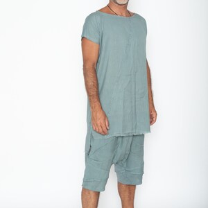 May include: A teal two-piece outfit. The top is a loose tunic with short sleeves and a raw hem. The shorts are knee-length with a patchwork design. The clothing is made of a lightweight fabric. The outfit is suitable for warm weather.