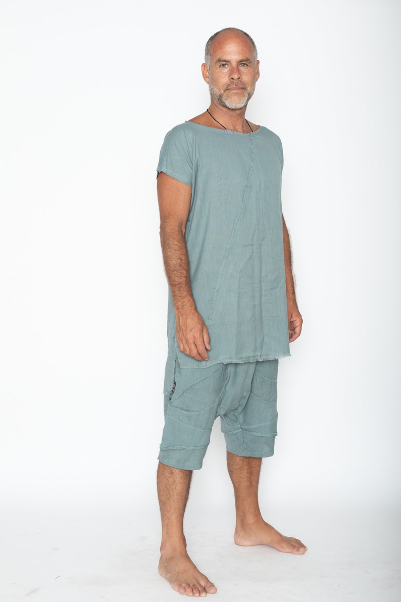 May include: A teal two-piece outfit. The top is a loose tunic with short sleeves and a raw hem. The shorts are knee-length with a patchwork design. The clothing is made of a lightweight fabric. The outfit is suitable for warm weather.