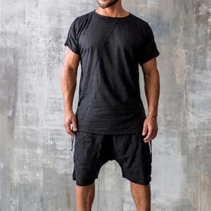 May include: Black t-shirt and shorts outfit. The short-sleeved shirt has a diagonal seam across the chest. The shorts have a drawstring waist. The person is wearing black high-top boots.