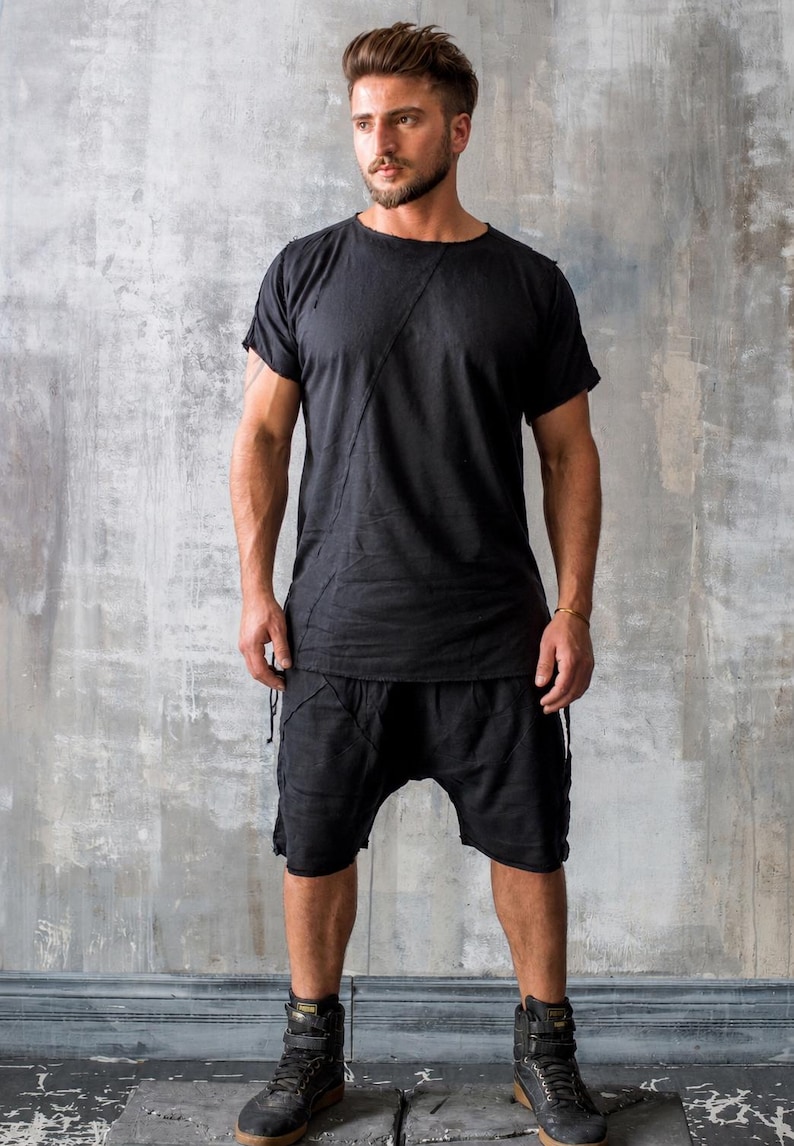 May include: Black t-shirt and shorts outfit. The short-sleeved shirt has a diagonal seam across the chest. The shorts have a drawstring waist. The person is wearing black high-top boots.