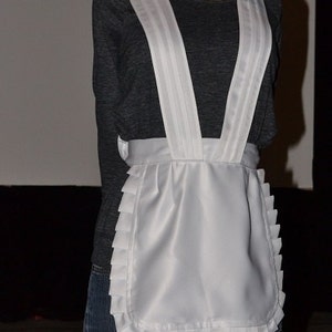 May include: A white apron with a ruffled hem and wide straps. The apron is made of a smooth, silky fabric and has a simple, classic design.