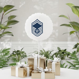 May include: A white balloon with a blue Air Force rank insignia printed on it. The balloon is tied to a white string and is floating above a table with three gold gift boxes.