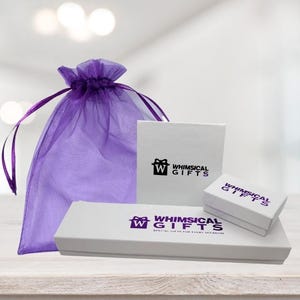 May include: A collection of gift boxes and a purple organza gift bag. The white boxes feature the text "WHIMSICAL GIFTS" in purple. The boxes are in various sizes, suggesting they are for jewelry or small gifts.