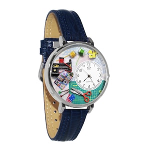 Könnte beinhalten: Silberfarbene Uhr mit blauem Lederarmband. Das Zifferblatt zeigt Illustrationen zum Thema Nähen, darunter eine Nähmaschine, Garnrollen, eine Schere und ein Quilt. Die Uhr hat ein Quarzwerk.
