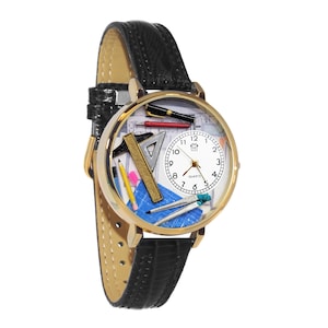 Op de afbeelding: Een goudkleurig polshorloge met een zwarte leren band. De wijzerplaat van het horloge toont tekengereedschap, waaronder een liniaal, een driehoek en pennen. Het horloge heeft een witte wijzerplaat met zwarte cijfers en wijzers, en het woord "QUARTZ" staat onderaan gedrukt.