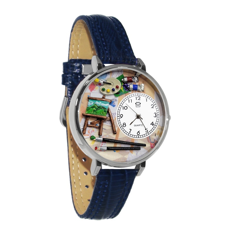 May include: A silver-toned wristwatch with a blue leather band. The watch face features a miniature painting scene with an easel, paint tubes, brushes, and a palette. The watch has a white face with black numerals and hands.