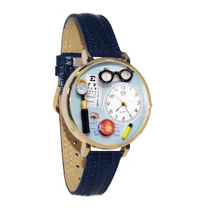 May include: A gold-toned quartz wristwatch with a light blue face featuring eye exam-related graphics. The watch has a blue leather band and includes a miniature eye chart, glasses, and an eye illustration.
