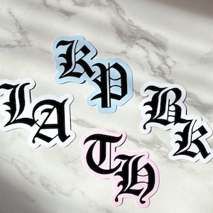 May include: Four stickers with black gothic lettering on different colored backgrounds. The letters spell out "LA", "BK", "TH", and "KP".