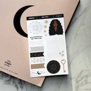 May include: A sheet of black and white stickers with a celestial theme. The stickers feature a woman with long black hair, a crescent moon, stars, and a key. The text on the sheet reads "Manifest", "Declutter", "Manifesting My Dreams", and "Little Magic Prints".