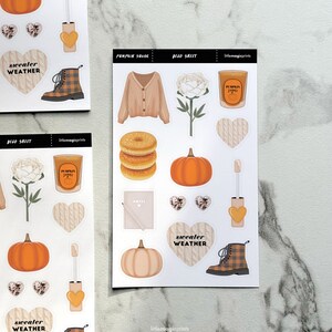 May include: Decorative sticker sheets featuring fall-themed illustrations. Includes images of a cardigan, pumpkin, donuts, candle, boots, and hearts. The text "Sweater Weather" is visible on some stickers. The sheets are labeled "Pumpkin Sugar" and "Deco Sheet".