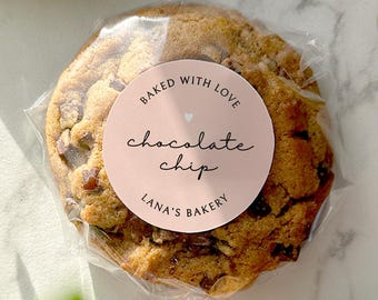May include: A pink and white sticker with the text "Baked with Love Chocolate Chip Lana's Bakery" on a chocolate chip cookie.