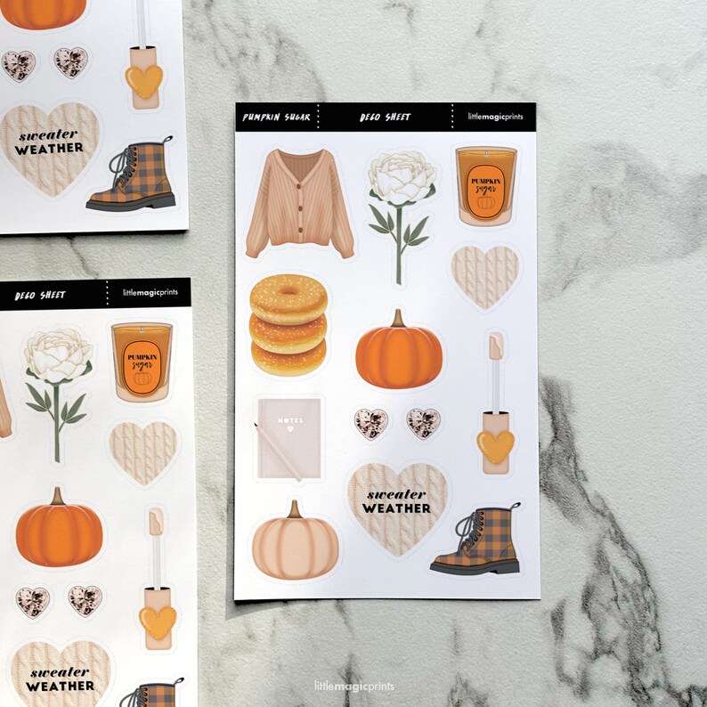 May include: Decorative sticker sheets featuring fall-themed illustrations. Includes images of a cardigan, pumpkin, donuts, candle, boots, and hearts. The text "Sweater Weather" is visible on some stickers. The sheets are labeled "Pumpkin Sugar" and "Deco Sheet".