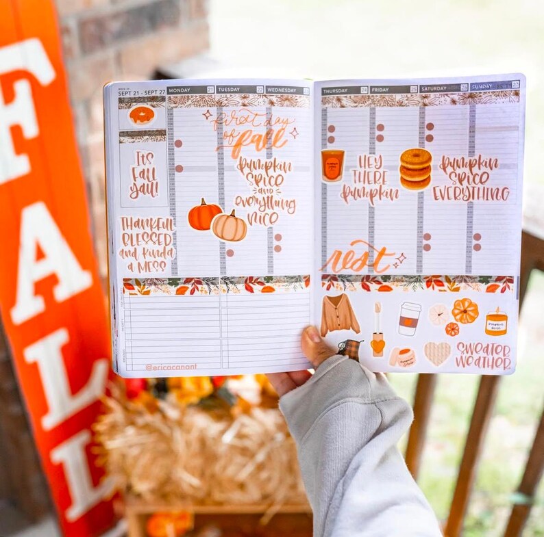 May include: Open planner with fall-themed stickers and handwritten text. The planner includes phrases like "It's Fall Y'all!" and "Pumpkin Spice Everything." Decorative elements include pumpkins, leaves, and coffee cups. The planner is open to the week of September 21-27.