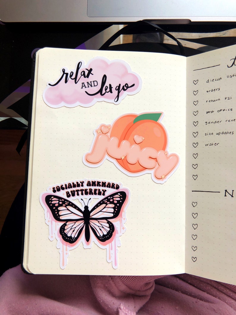 May include: A planner page with three stickers. The first sticker is a pink cloud with the text "relax and let go" in black. The second sticker is a peach with a heart on it. The third sticker is a pink butterfly with black wings and the text "socially awkward butterfly" in black.