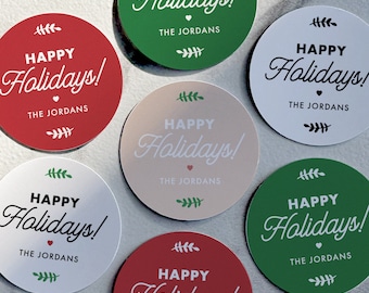 May include: Round Christmas stickers in red, green, white, and beige. Each sticker features the words "HAPPY Holidays!" in a script font, with "THE JORDANS" below. Decorative sprigs and a heart are included in the design.