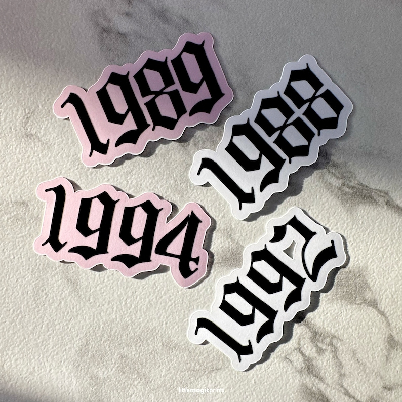 May include: Four stickers with different years printed in black gothic font on a white background. The years are 1999, 1998, 1994, and 1992. The stickers are on a light gray marble surface.