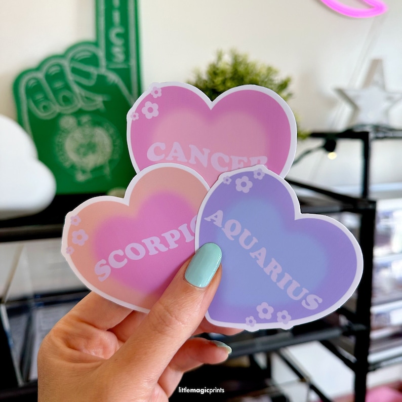 May include: Three heart-shaped stickers with zodiac signs. The stickers are pink, peach, and purple with white text. The text on the stickers reads "Cancer", "Scorpio", and "Aquarius".