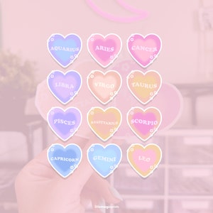 May include: Twelve heart-shaped stickers with the astrological signs of the zodiac. Each sticker is a different pastel color with white outlines and white text. The signs are: Aquarius, Aries, Cancer, Libra, Virgo, Taurus, Pisces, Sagittarius, Scorpio, Capricorn, Gemini, and Leo.