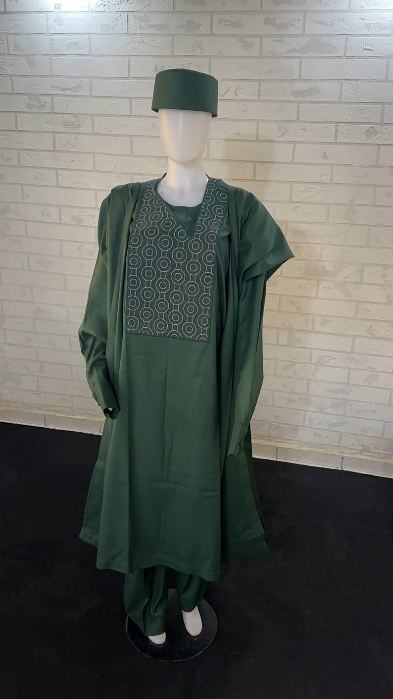 Pode incluir: Um traje tradicional masculino verde com um padr&atilde;o geom&eacute;trico no peito. O traje inclui uma t&uacute;nica longa, cal&ccedil;as e um chap&eacute;u.