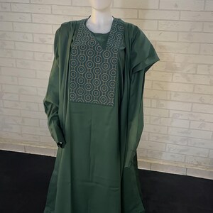 Pode incluir: Um conjunto de tr&ecirc;s pe&ccedil;as verde escuro com um padr&atilde;o geom&eacute;trico no peito. O conjunto inclui uma camisa de manga comprida, cal&ccedil;as e um chap&eacute;u.