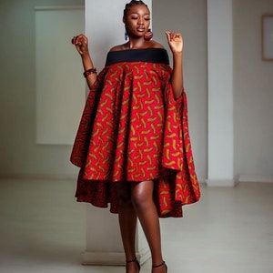 Pode incluir: Um vestido vermelho e dourado com decote ombro a ombro e uma faixa preta na cintura. O vestido tem uma bainha alta-baixa e &eacute; usado por uma pessoa de pele escura.