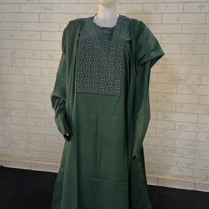 Pode incluir: Um conjunto de tr&ecirc;s pe&ccedil;as verde escuro com um padr&atilde;o geom&eacute;trico no peito. O conjunto inclui uma camisa de manga comprida, cal&ccedil;as e um chap&eacute;u.