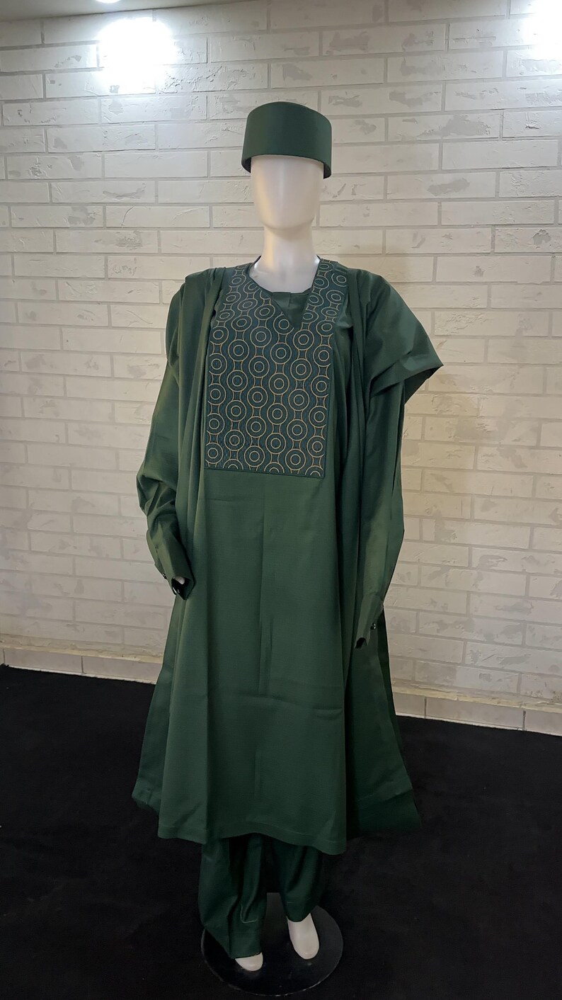 Pode incluir: Um conjunto de tr&ecirc;s pe&ccedil;as verde escuro com um padr&atilde;o geom&eacute;trico no peito. O conjunto inclui uma camisa de manga comprida, cal&ccedil;as e um chap&eacute;u.