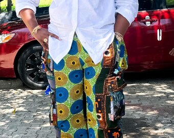 Puede incluir: Una persona con una camisa blanca y pantalones estampados con círculos azules, amarillos y verdes y formas geométricas. Los pantalones tienen una pernera ancha y un diseño único.