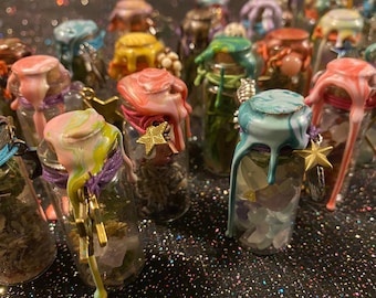 May include: A collection of small glass bottles with cork stoppers sealed with colorful, dripping wax. Each bottle contains various dried herbs, small crystals, or stones, and is adorned with a metallic star charm tied with colored string.