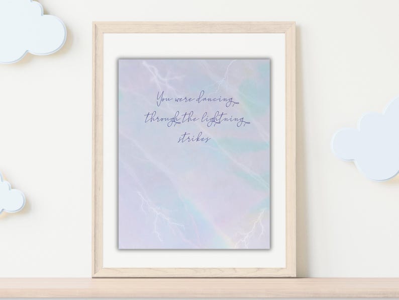 K&ouml;nnte beinhalten: Gerahmter Druck mit dem Schriftzug "You were dancing through the lightning strikes" in zarter Schrift. Der Hintergrund hat einen weichen Aquarell-Effekt mit Pastellt&ouml;nen von Blau, Lila und Gr&uuml;n, mit wei&szlig;en Blitzillustrationen.