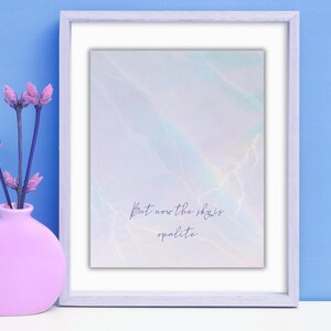 K&ouml;nnte beinhalten: Ein gerahmter Kunstdruck mit einem weichen, abstrakten Design in Pastellfarben. Der Druck zeigt den Text "But now the sky is opalite". Links vom Rahmen steht eine rosa Vase mit lila Blumen vor blauem Hintergrund.