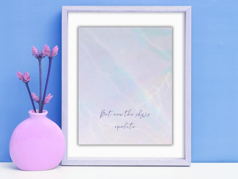 K&ouml;nnte beinhalten: Ein gerahmter Kunstdruck mit einem weichen, abstrakten Design in Pastellfarben. Der Druck zeigt den Text "But now the sky is opalite". Links vom Rahmen steht eine rosa Vase mit lila Blumen vor blauem Hintergrund.