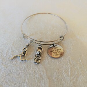 May include: A silver bangle bracelet with three charms: a running figure, a shoe, and a round charm with the text "I run like a girl Try to keep up".