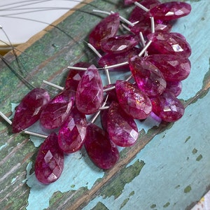 Può includere: Una collezione di pietre preziose rosa a forma di goccia con una finitura sfaccettata. Le pietre preziose sono infilate su fili d'argento e sono pronte per essere utilizzate nella creazione di gioielli.