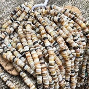 May include: A strand of white, brown, and black shell beads. The beads are round and flat, and they are strung together in a long, continuous strand. The beads are arranged in a random pattern, and they create a beautiful and unique look.
