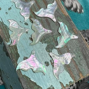 Op de afbeelding: Zeven iriserende witte parelmoer zeemeerminstaartvormen. De staarten zijn allemaal van verschillende grootte en vorm en hebben een parelmoerglans.