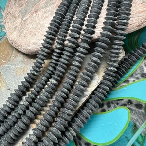 May include: A strand of dark grey, faceted, wooden beads. The beads are arranged in a row and are all the same size and shape. The beads are smooth and have a natural, rustic look.