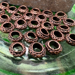 May include: A close-up of a group of copper-colored metal rings with a decorative design. The rings are arranged in a circular pattern on a green surface.